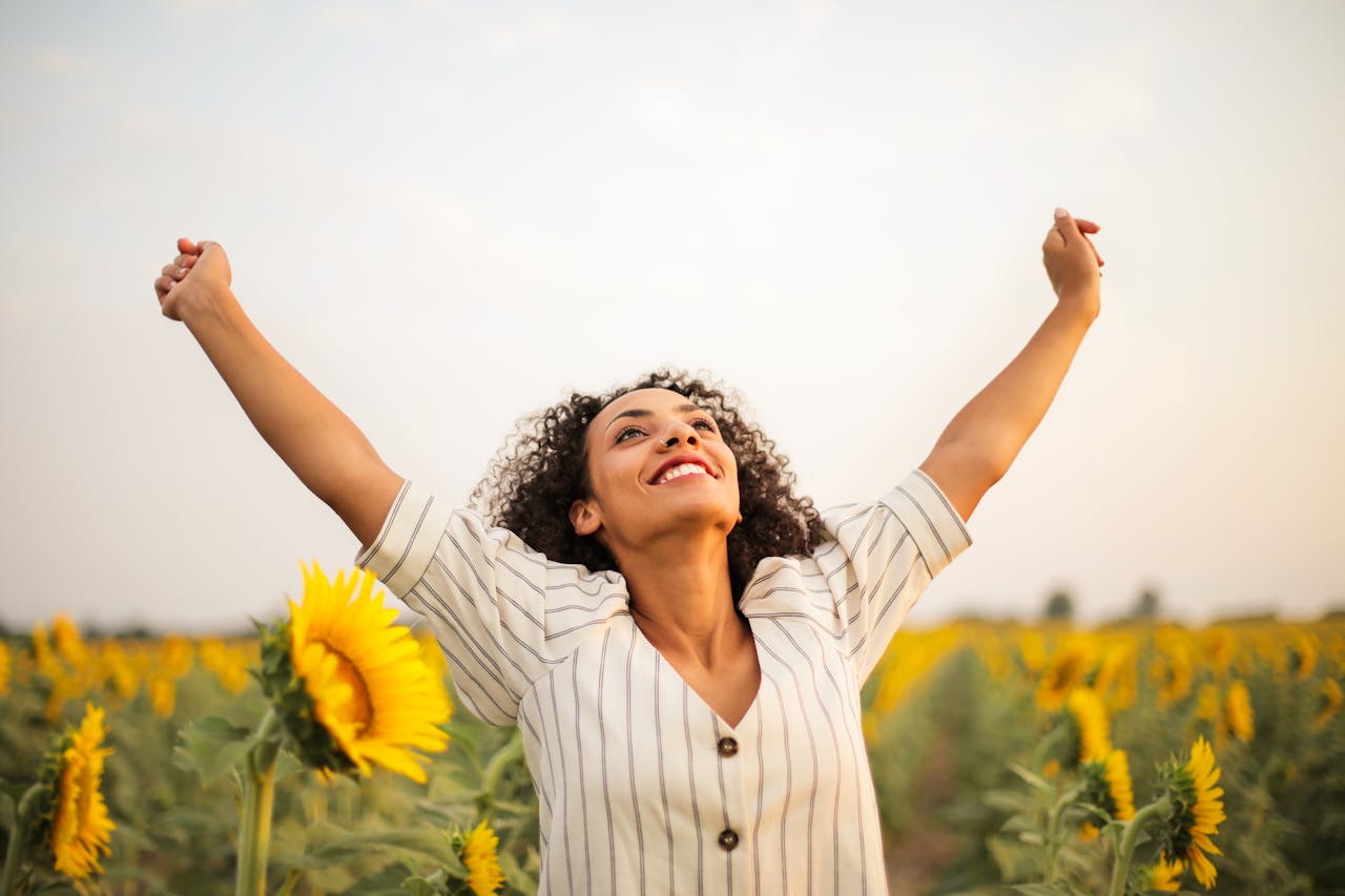 A woman raising her hand up joyfully in the middle of a sunflower field.